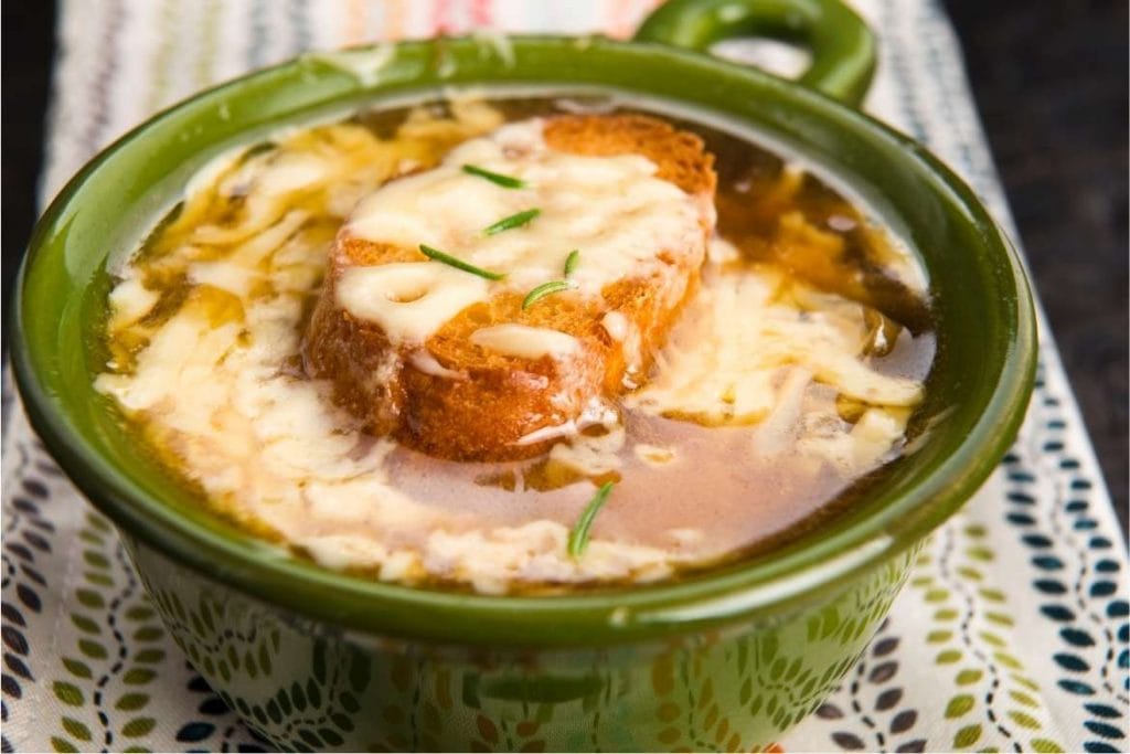 french onion soup in a green bowl with a slice of bread and melted cheese on top