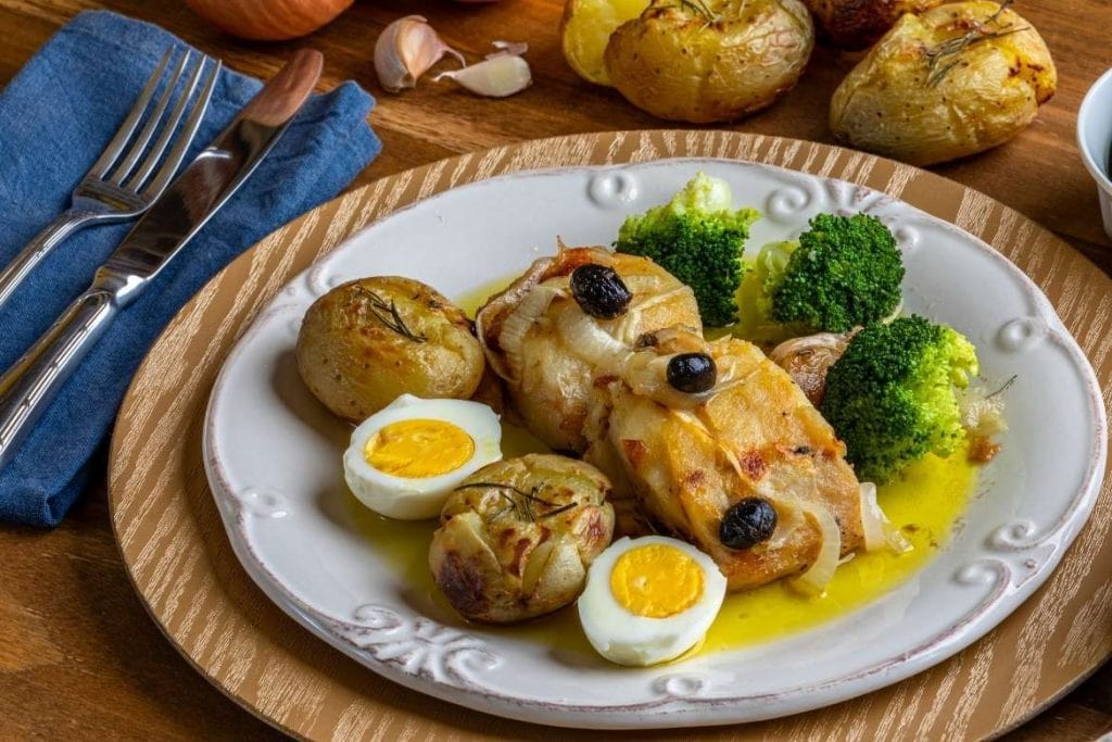 bacalhau à lagareiro no prato com azeite ovos cozidos e brócolis - um dos principais pratos com bacalhau em Portugal