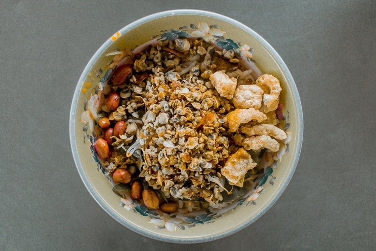 a bowl with Com Hen, one of Hue City's typical Vietnamese food made with clams rice, peanuts, and fried pork skin