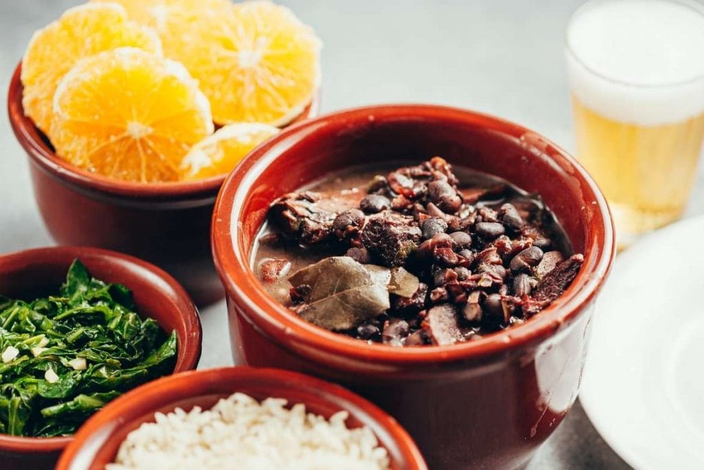 a traditional brazilian feijoada with side dishes including collard greens, rice, pork meat, beans, orange and more