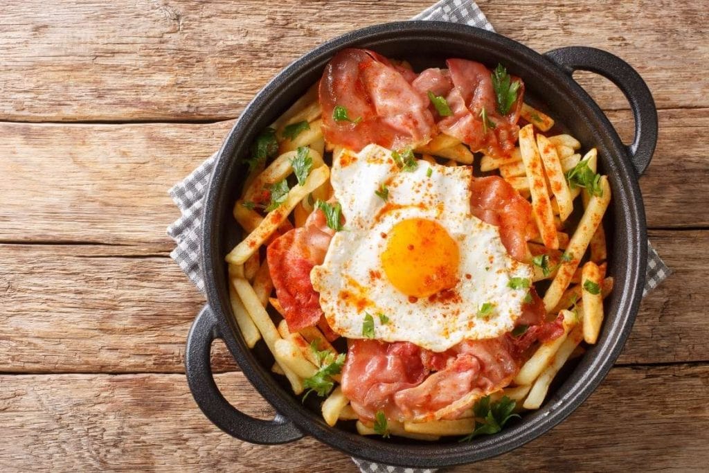 huevos rotos com batatas fritas presunto cru e ovos fritos por cima como uma típica comida espanhola e tapas