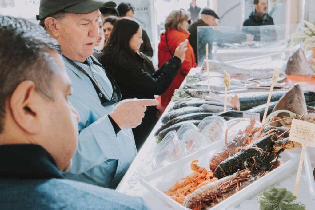 um homem, viajante olhando para frutos do mar frescos em uma barraca de mercado durante um passeio gastronômico a pé pela comida e cultura em Lisboa