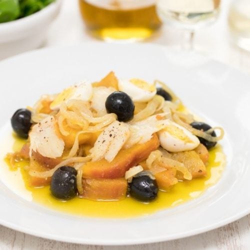 white plate with bacalhau gomes de sá made with potatoes, olives, onion and eggs