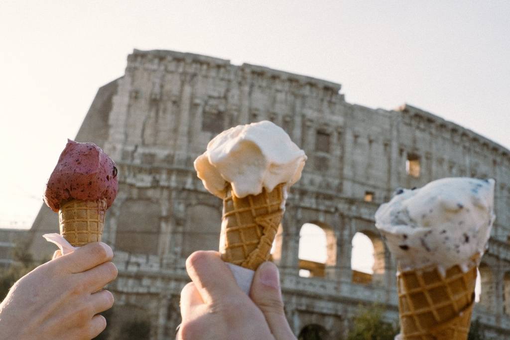 mãos segurando 3 gelatos em frente ao Coliseu em Roma